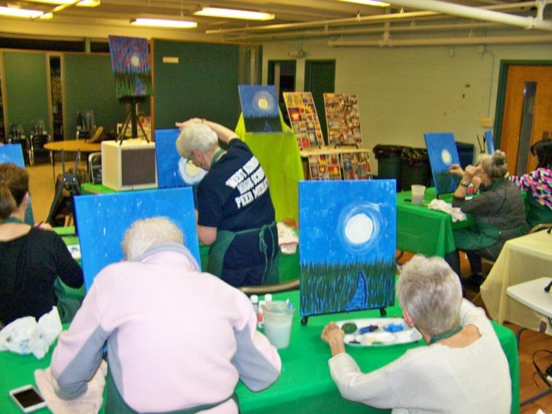 Several painters at tables working on matching moonlit landscape canvases