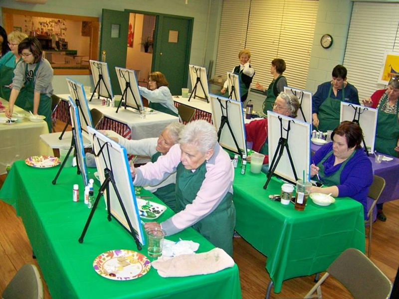 Painters at easels in a community hall during a guided paint night