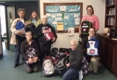 Volunteers holding filled backpacks for neighborhood children