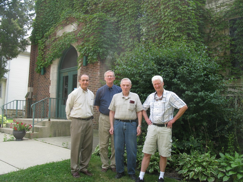 Four men standing on the lawn in front of the ivy-covered church entrance